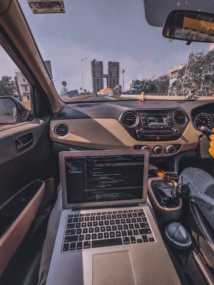 Car interior with laptop on dashboard, city view outside, sunny day.